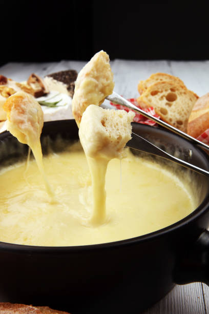 istock Gourmet Swiss fondue dinner on a winter evening with assorted cheeses on a board alongside a heated pot of cheese fondue with two forks dipping 1185736270