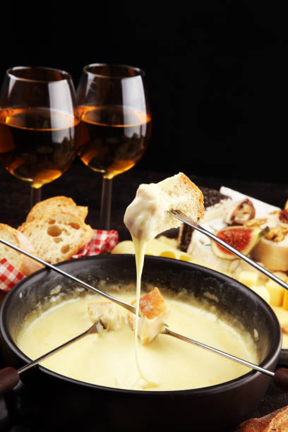 istock Gourmet Swiss fondue dinner on a winter evening with assorted cheeses on a board alongside a heated pot of cheese fondue with two forks dipping 1185736331