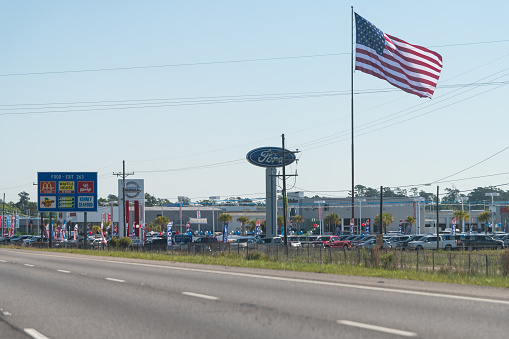 Slidell, USA - April 24, 2018: Highway i10 interstate 10 near New Orleans with sign for Ford dealership and large American Flag