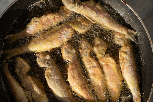 Close up photo of ed mullet fish in cooking oil being fried. Shot from a high angle viewpoint. No people are seen in frame. Shot with a full frame mirrorless camera.