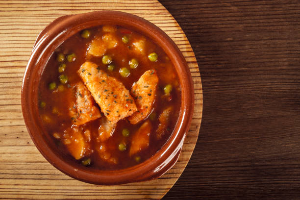 Top view of a clay pot with a delicious fish stew with peas and cooked potatoes on a wooden plate on a rustic table. Healthy fish soup. Homemade food. Hot food, freshly made stock photo
