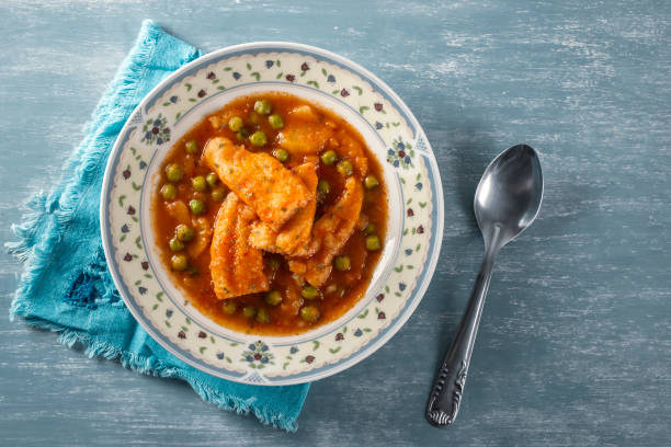 Top view of a delicious fish stew with peas and cooked potatoes on a vintage plate, on a blue napkin, with a vintage spoon on a rustic blue wooden table. Healthy fish soup. Homemade food. Hot food stock photo