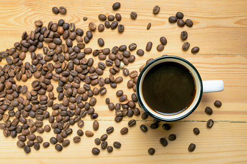 Roasted coffee beans and a mug of coffee stands directly on wooden table