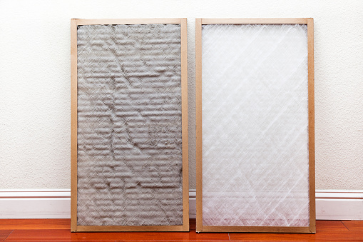 Old and New air conditioner filter next to each other leaning against the wall