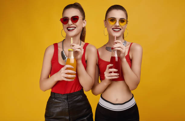 dos elegantes chicas gemelas hipster glamor en la moda red top con bebida de cóctel - women sunglasses little girls glamour fotografías e imágenes de stock