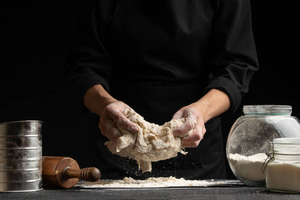 istock The cook is working making the dough, sprinkle flour kneading it in his hands on a black background. Freezing in motion. Cooking baking, culinary background, recipe book, menu 1185765595