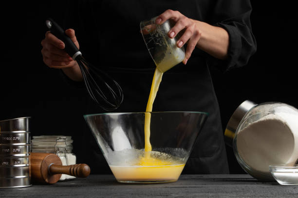 istock a pastry chef or baker cooks dough, pours yeast into a container, for making sweets, rolls or Italian pizza or pasta. Freezes in motion. On a black background, horizontal photo 1185767501