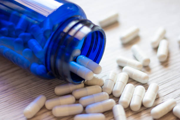 istock Blue medicine bottle with white pill capsules thrown on the table 1185769208