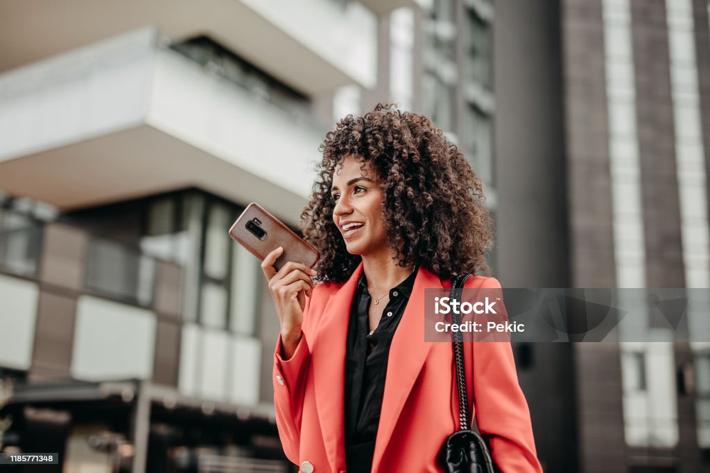 Sending voice messages on the move Beautiful businesswoman in read coat on her way to work place Voice Stock Photo