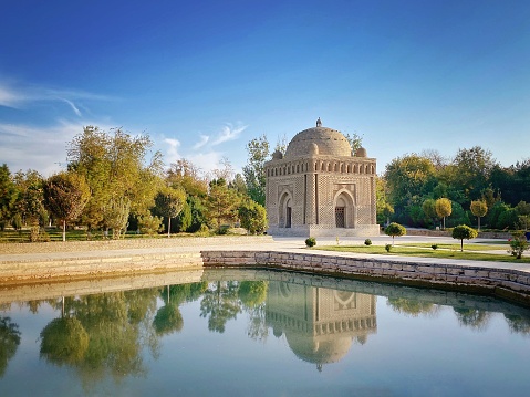 Ismael Samani Mausoleum reflecting in tranquil water pond water on a sunny day. Samoni Park, Bukhara, Uzbekistan, Central Asia