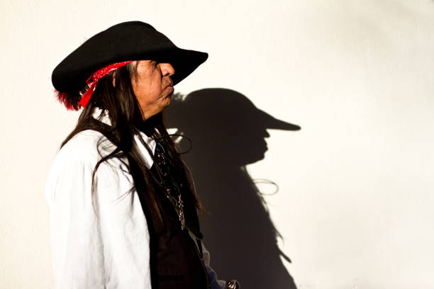 Santa Fe, NM: A Native American man in a black hat walks by a sunny white wall in downtown Santa Fe, projecting his silhouette onto the wall.