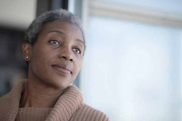 Middle Aged African Woman Reflecting stock photo A beautiful, middle aged African woman rests her head against a window as she leans against it with her back.  She has a neutral expression on her face as she is deep in thought and reflection.  She is wearing a casual and comfortable sweater in this head shot. 40 49 years stock pictures, royalty-free photos & images
