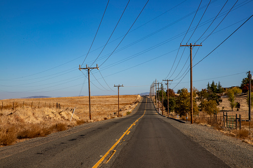 Center yellow striped straight county road bordered by power lines.  Rich blue sky.