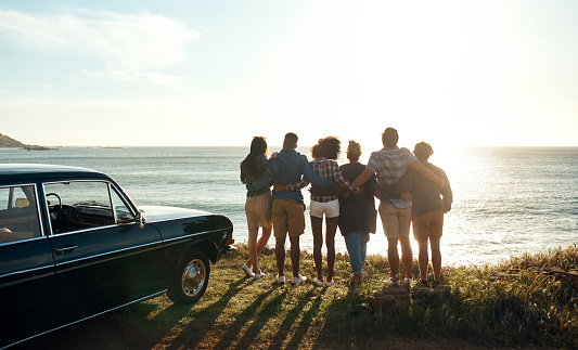 Shot of a group of young friends watching the sunset on a road trip along the coast
