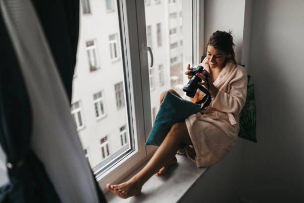 istock Beautiful young woman with camera on window sill 1185802818