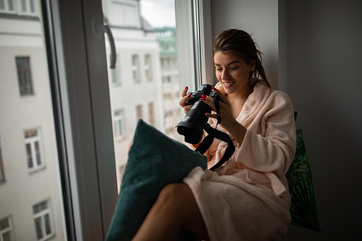 Beautiful young woman with camera on window sill