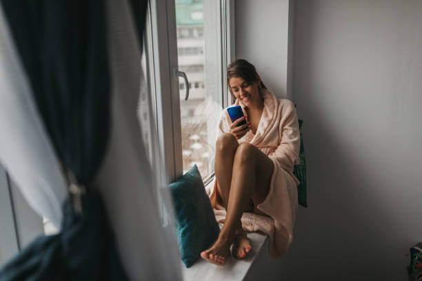 istock Woman texting on the window sill 1185804012