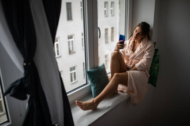 istock Woman texting on the window sill 1185804082