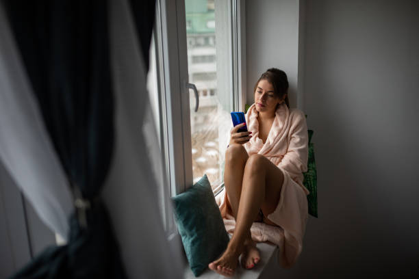 istock Woman texting on the window sill 1185804386