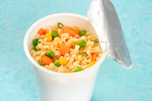 istock Ramen cup close-up, instant soba noodles in a plastic cup with vegetables, on a blue background 1185809043