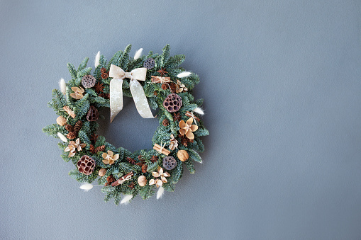 Christmas wreath made of natural fir branches  hanging on a grey wall.  Wreath with natural ornaments: bumps, walnuts, cinnamon, cones. New year and winter holidays. Christmas decor. Copy space