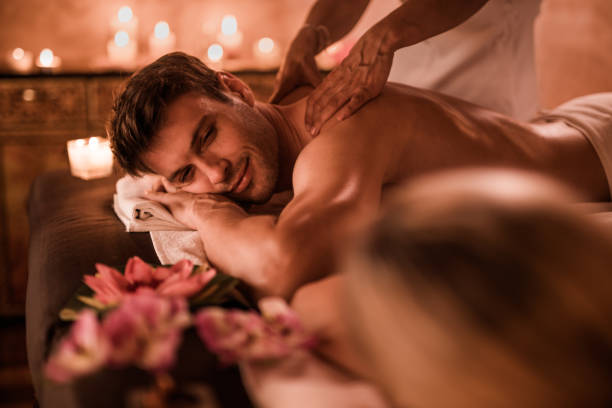 Young man having relaxing massage while being at health spa with his girlfriend. Focus is on man.