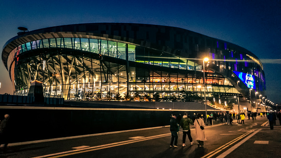London, UK - 22 October, 2019: color image depicting the ultra modern architecture of the brand new Tottenham Hotspur football stadium iiluminated at night in London, UK. Tottenham Hotspur Stadium is a stadium that serves as the home ground for Tottenham Hotspur in north London, replacing the club's previous stadium, White Hart Lane. It has a capacity of 62,062, making it one of the largest in the Premier League and the largest for a club stadium in London. It is designed to be a multi-purpose stadium and features a world's-first dividing, retractable football pitch, that reveals a synthetic turf pitch underneath for NFL London Games, concerts and other events. Room for copy space.