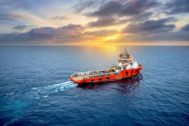 Supply boat offshore oil rig on loading operation with cloudy sky and blue ocean background