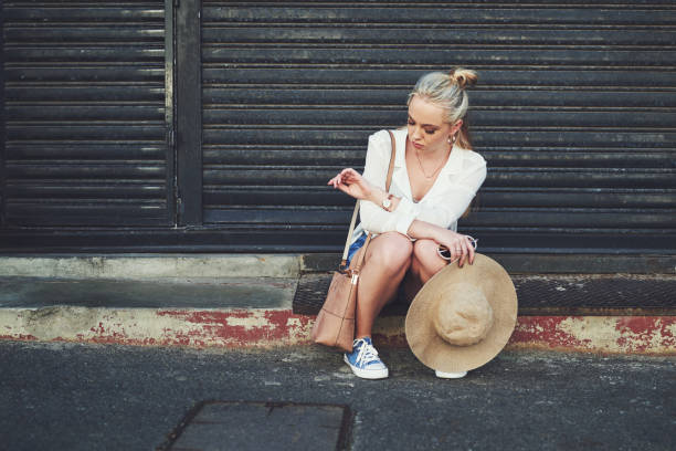 Full length shot of an upset young woman checking the time on her wristwatch while sitting outdoors