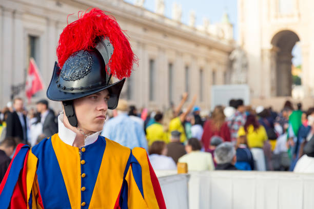 Vatican City, Italy. October 13, 2019. A member of the Pontifical Swiss Guard close to Saint Peter’s Basilica at the Vatican City with sunset light. Apostolic Palace buildings.