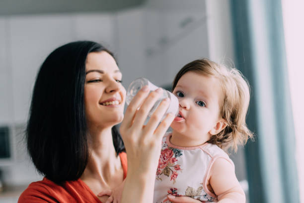 istock Young mother feeds her baby from bottle in kitchen 1185834835