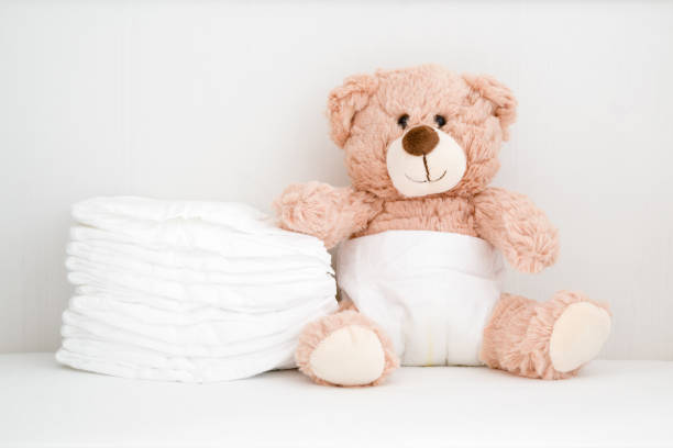 istock Brown teddy bear sitting in baby bed. Stack of white diapers. Front view. Closeup. 1185835441