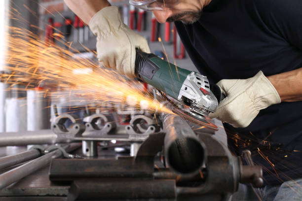 man work in home workshop garage with angle grinder, goggles and construction gloves, sanding metal makes sparks closeup, diy and craft concept