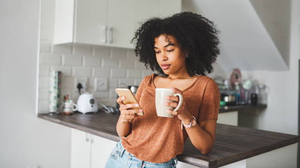 When the wifi’s good the day’s going to be good Shot of a young woman using a smartphone and having coffee in the kitchen at home leaning photos stock pictures, royalty-free photos & images