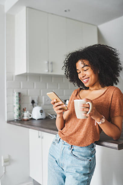 Turn on the day with coffee and social media Shot of a young woman using a smartphone and having coffee in the kitchen at home mobile phone text messaging telephone women stock pictures, royalty-free photos & images