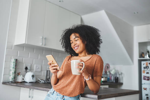 Everybody loves those good morning messages Shot of a young woman using a smartphone and having coffee in the kitchen at home mug photos stock pictures, royalty-free photos & images
