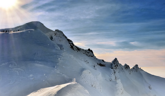 luz solar en pequeñas silouettes de excursionistas escalando una montaña nevada photo