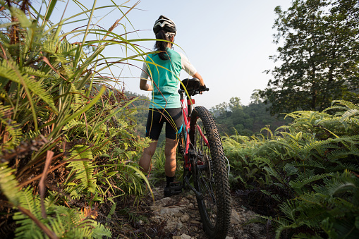 Cross country biking woman cyclist with mountain bike on tropical forest trail looking at the view