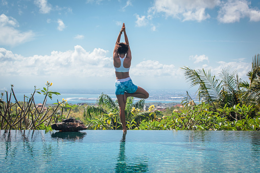 Young woman practicing yoga pose ashtanga hatha asana on the edge of infinity pool with breathtaking view at the villa in Bali