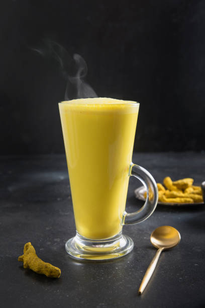 bicchiere di latte di curcuma dorata ayurvedico con polvere di curcuma su nero. colpo verticale. - cardamom indian culture food spice foto e immagini stock