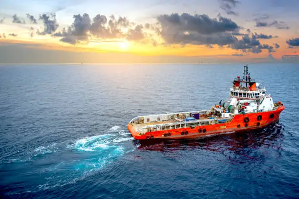 Supply boat offshore oil rig on loading operation with cloudy sky and blue ocean background.