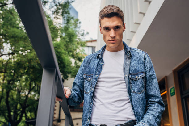 Handsome young man in denim shirt standing outdoors.