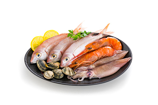 Food: group of healthy fresh raw seafood in a black plate isolated on white background. The composition includes fish, shrimps, squid and various clams. Predominant colors are red and white. XXXL 42Mp studio photo taken with Sony A7rii and Sony FE 90mm f2.8 macro G OSS lens