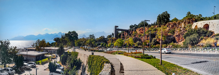 Panoramic view of Konyaalti Beach and rocky cliff with a park on top in Antalya, Turkey. Bright colorful landscape with sea, mountains and tropical vegetation on a sunny summer-autumn day