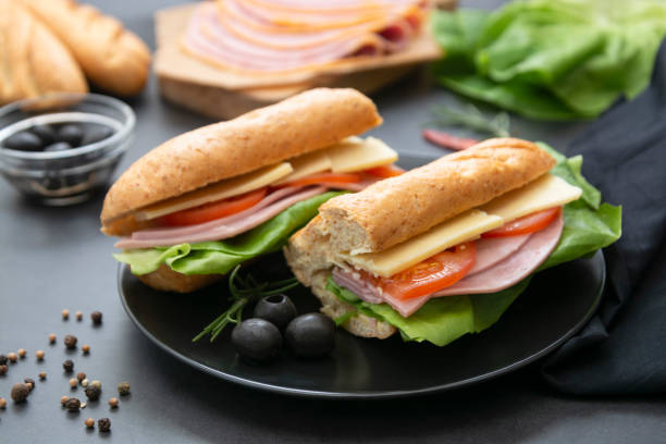 kanapka z chlebem bagietkowym, szynką, sałatą, pomidorem na ciemnym tle. śniadanie lub fast food. - bun salad ham rolled up zdjęcia i obrazy z banku zdjęć