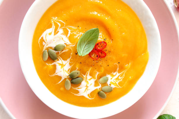 istock Pumpkin and carrots soup with cream and basil on white background. 1185853631
