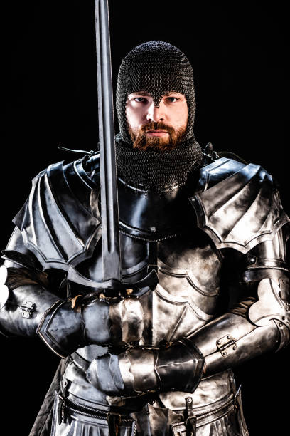 istock handsome knight in armor looking at camera and holding sword isolated on black 1185855374