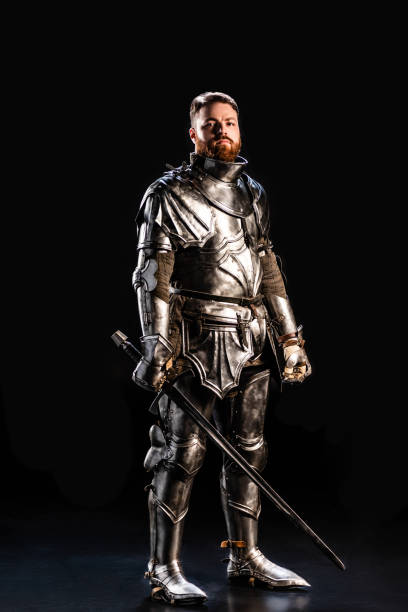 istock handsome knight in armor holding sword isolated on black 1185855409