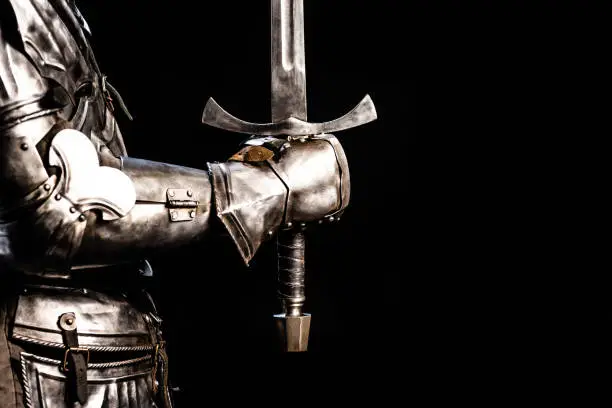 Photo of cropped view of knight in armor holding sword isolated on black