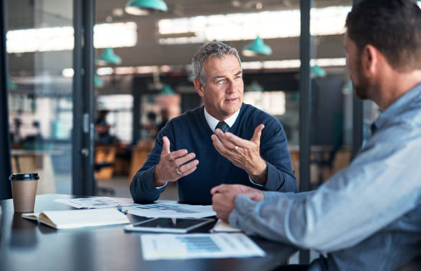 Explaining his vision to a colleague Shot of a mature businessman having a discussion with a colleague in an office manager stock pictures, royalty-free photos & images